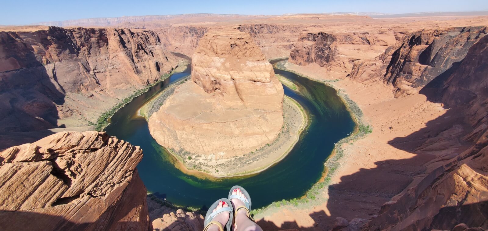 Photo of Horseshoe Bend, featuring feet hanging off the ledge.