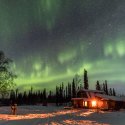 Green Northern Lights shine over a snow-covered cabin in Alaska