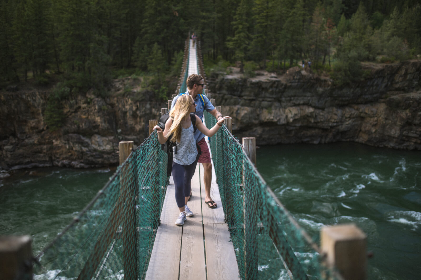 Visitors on a swinging bridge over a river in Glacier Country, Montana