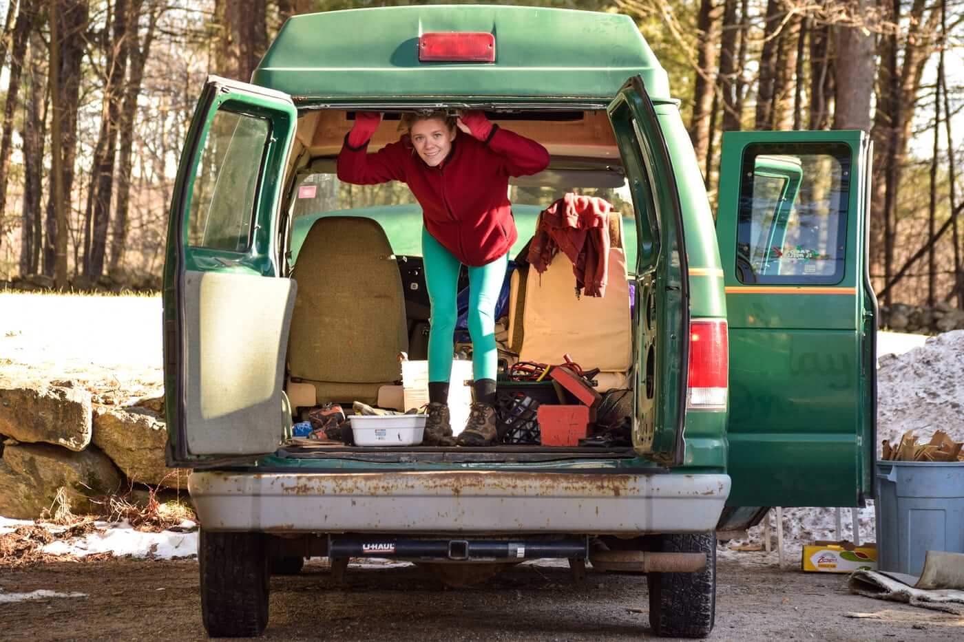 A woman living in her van swings open the double doors in the back of the van.