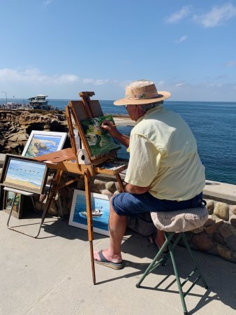 Artist Robert A. Higgins sitting seaside in San Diego, California, paintings images of the coast.