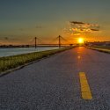 An open road leads to the sunset with the levee and bridge on the left.