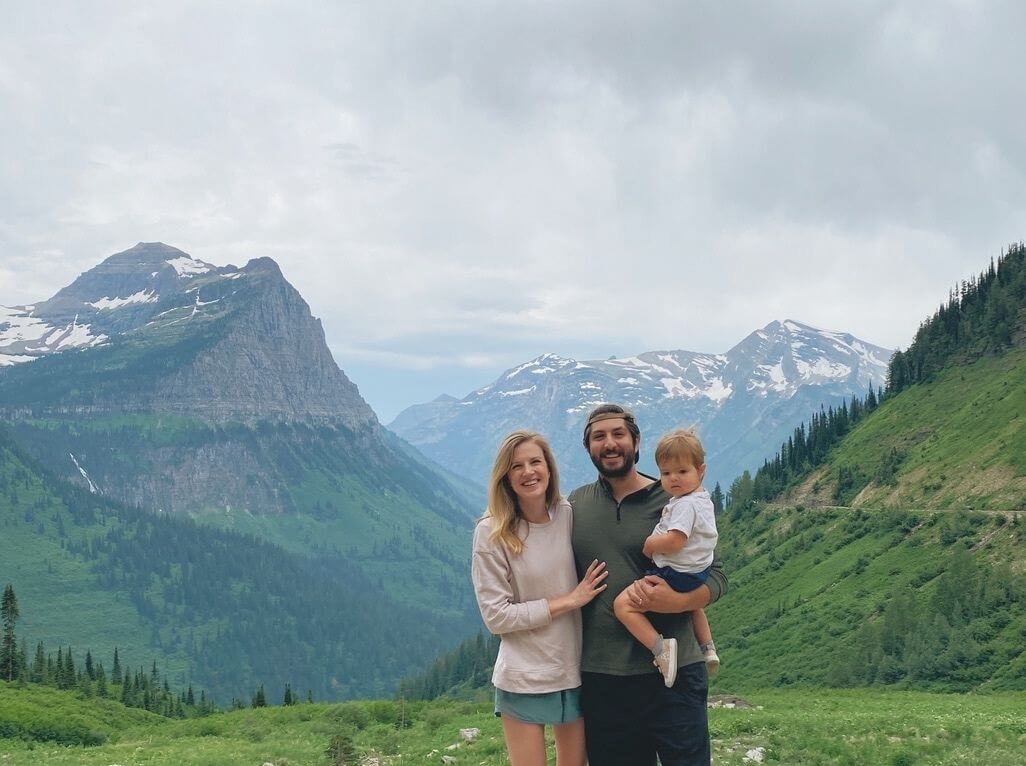 Parents with toddler posing on top of a mountain at Glacier National Park