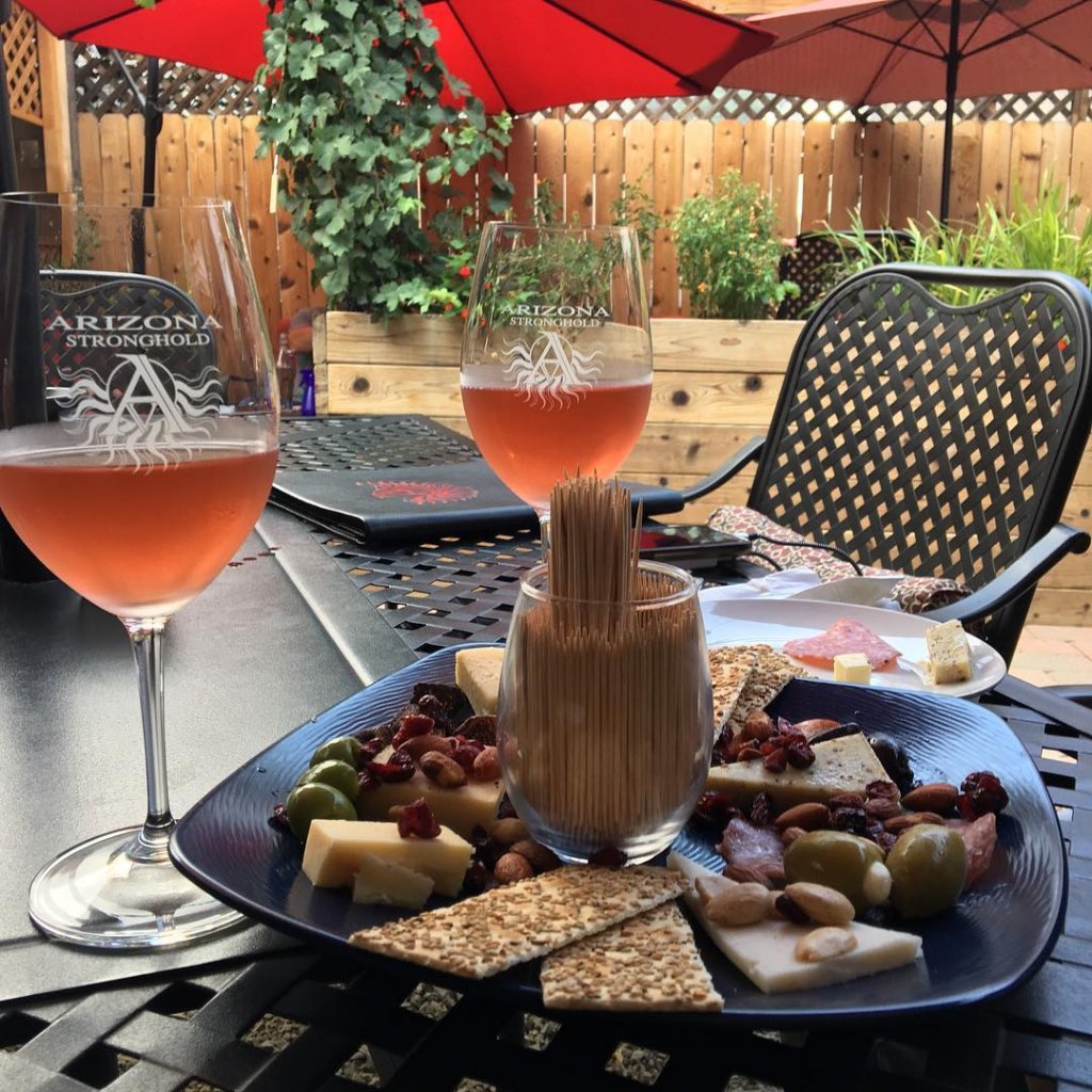 Two glasses of chilled wine sit adjacent to a charcuterie board on the patio of Arizona Stronghold Vineyards in Old Town Cottonwood, Arizona.