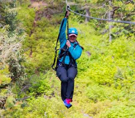 woman ziplining through a forest of trees at Tamarack Resort.