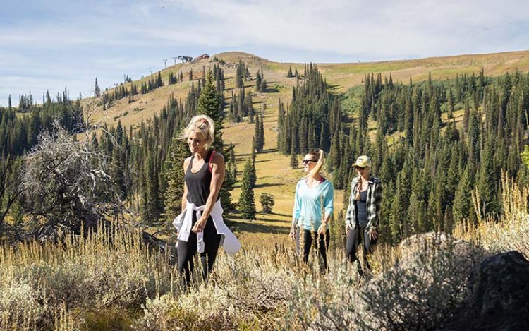 three women hiking at Tamarack Resort with a tree-covered hill in the background.