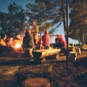 A group of people gather around a bonfire at a campsite at night.