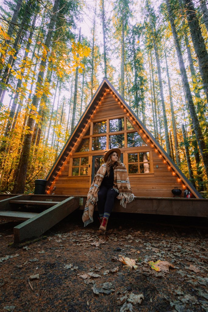 Photo of a women outside of a vacation rental house shaped like triangle in the woods. 