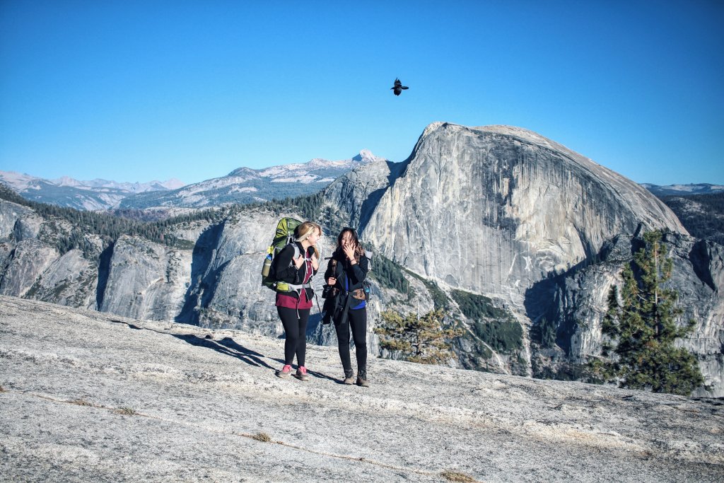 Two women laugh as they walk away from half dome