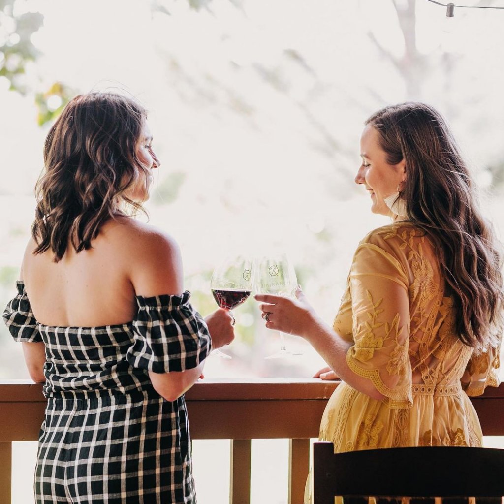 Two friends stand on the patio of D.A. Ranch Lodge & Estate Vineyards in Cornville, Arizona toasting with two glasses of wine.