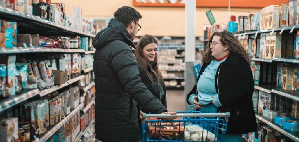 Two women and one man speaking in a grocery store aisle. 