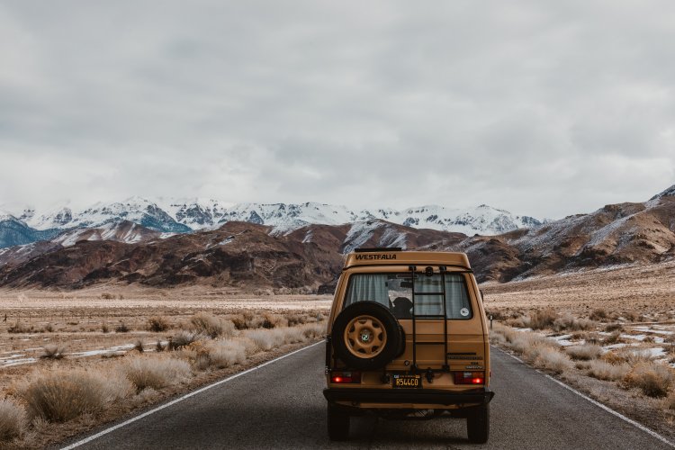 camper van traveling down open road with snow capped peaks in the distance