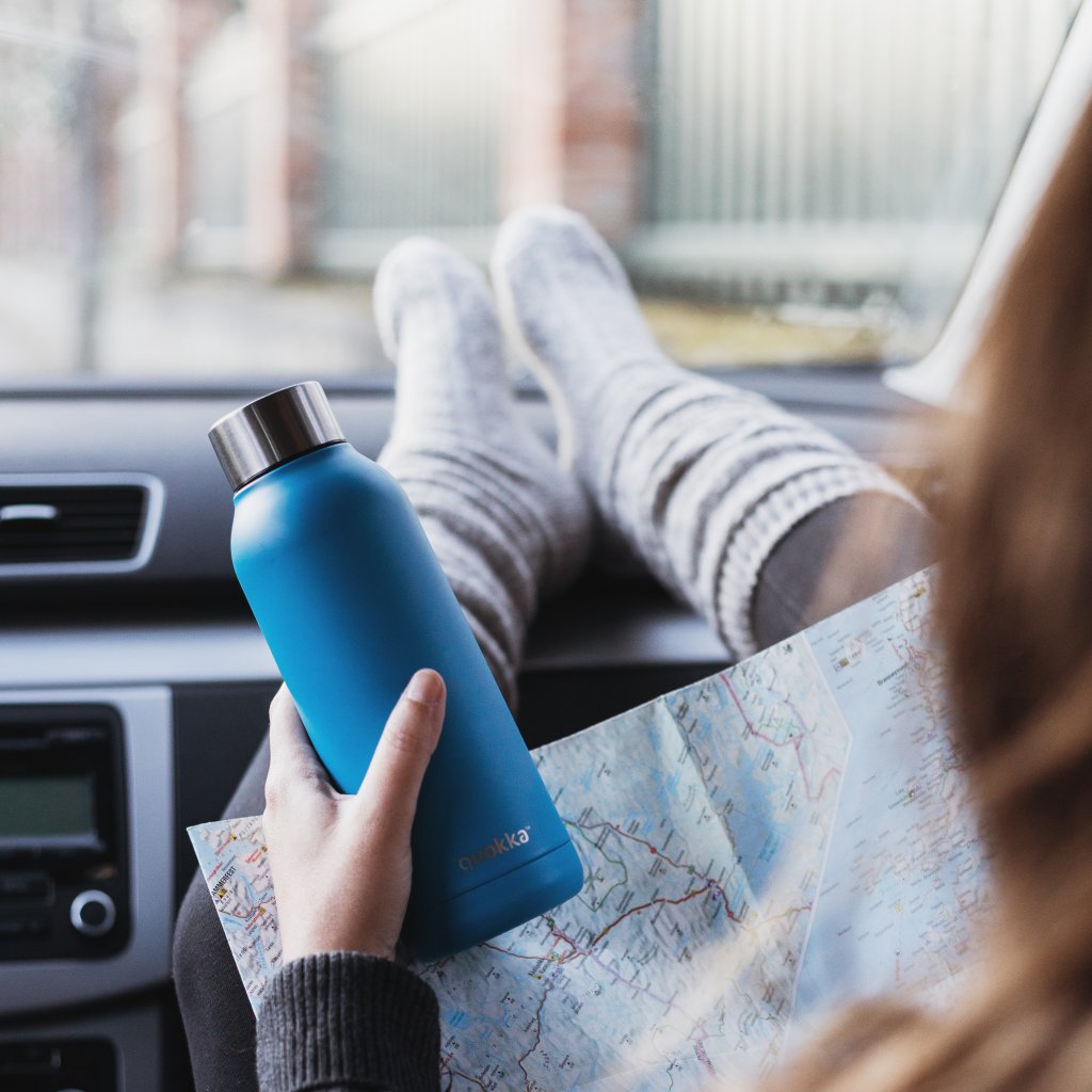 Women in passenger seat of car with legs on the dashboard, holding a map and a blue water bottle. 