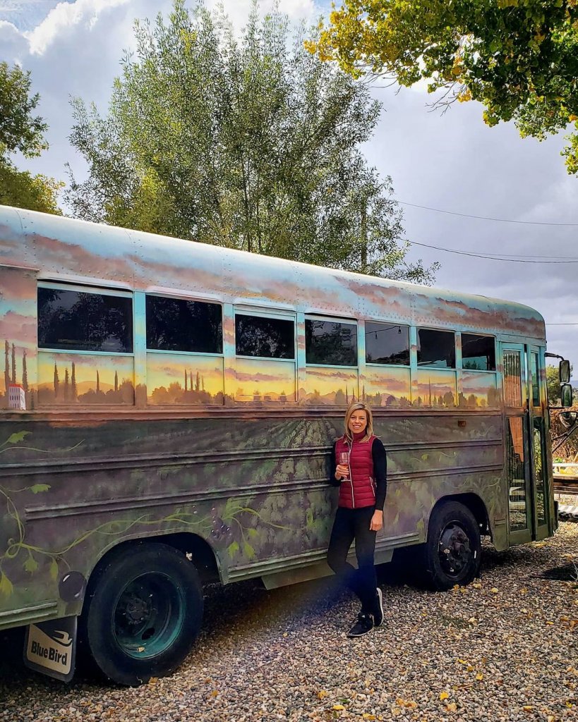 A patron of Clear Creek Vineyard & Winery in Camp Verde, Arizona, stands in front of bus painted to look like vineyards holding a glass of wine.