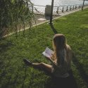 Photo of a girl reading a book sitting in grass.