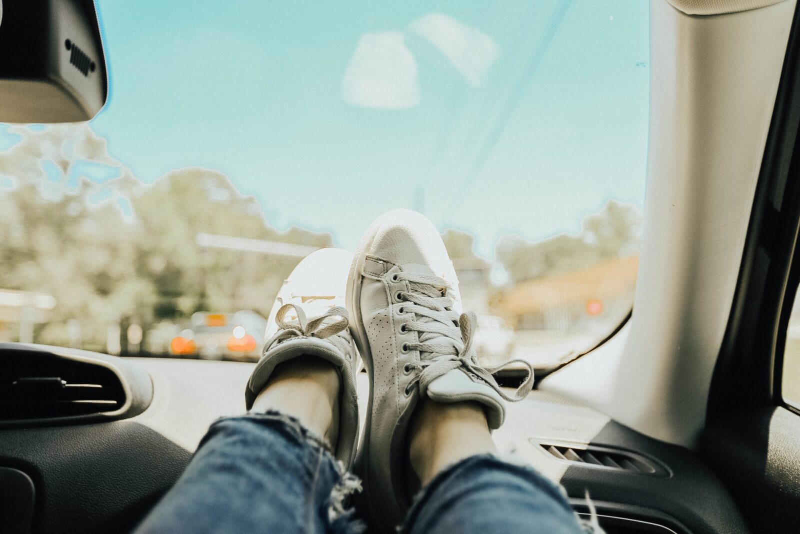 Someone wearing sneakers with their feet placed on top of the car dashboard.